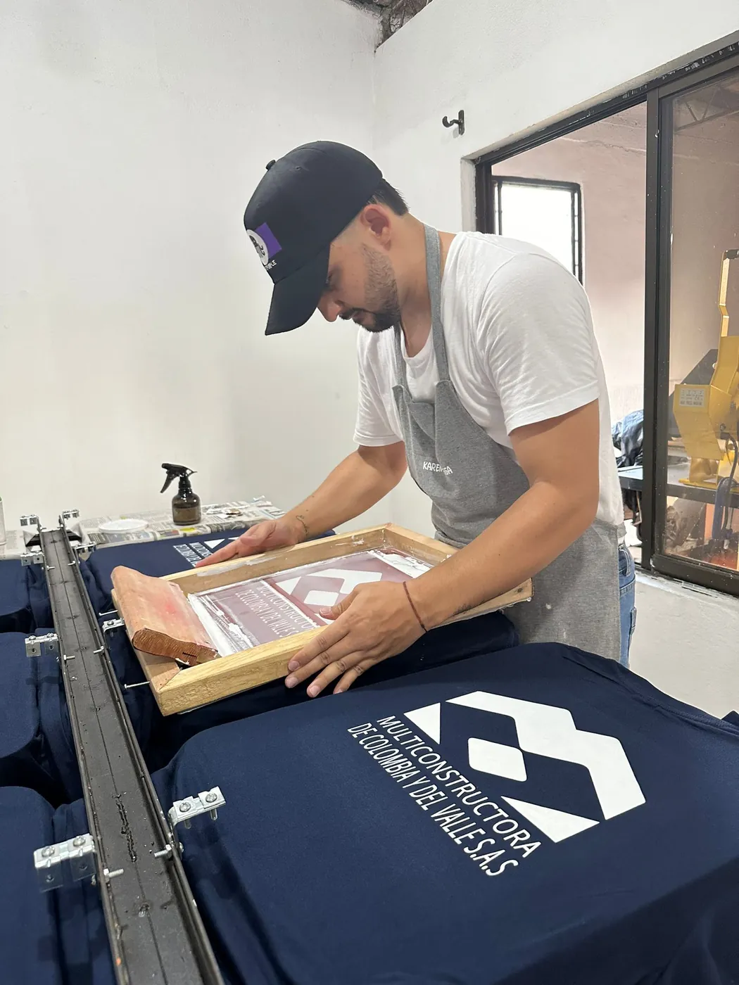 Integrante del taller estampando en serigrafía el logo de Multiconstructora de Colombia y del Valle S.A.S sobre camisetas azul oscuro